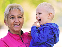 Natural Pharmaceuticals OmegaMarine Junior A mosolygós nagymama rózsaszín pulóverben örömmel öleli a kisgyermeket.